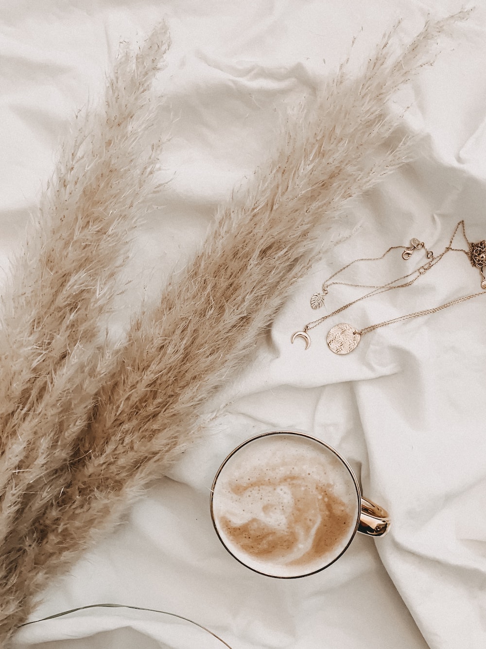 Styled flat-lay with coffee, jewelry, and pampas grass