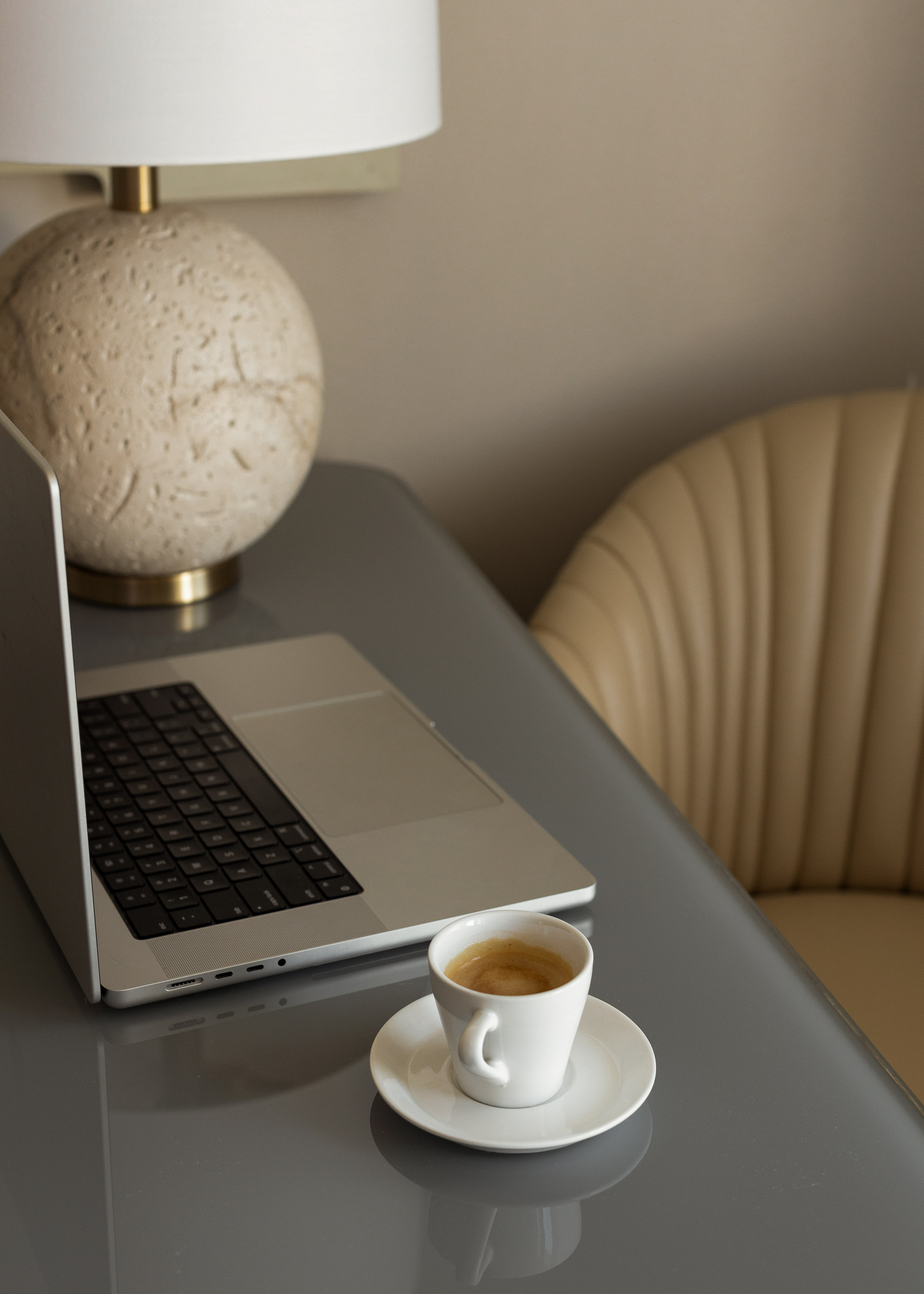 An open laptop and a fresh espresso on a sleek desk beside a stone lamp